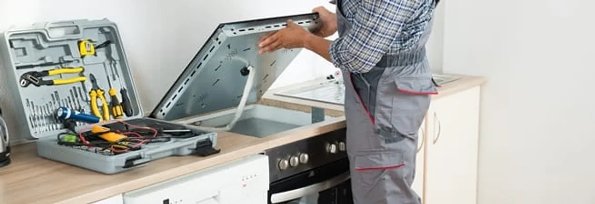Cooktop repair technician lifting a built-in stovetop for service in Little Rock, AR