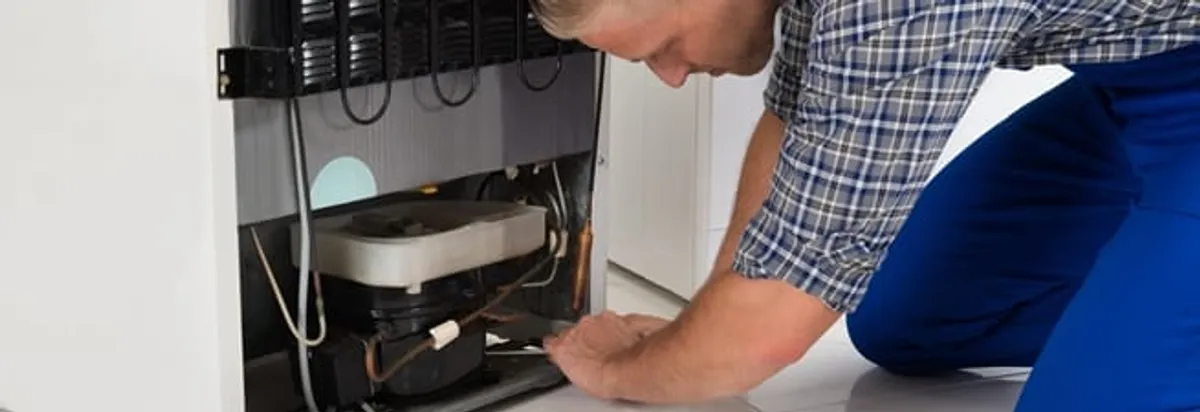 Refrigerator repair technician servicing the compressor and condenser area in Little Rock, AR
