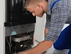 Refrigerator repair technician servicing the compressor and condenser area in Little Rock, AR